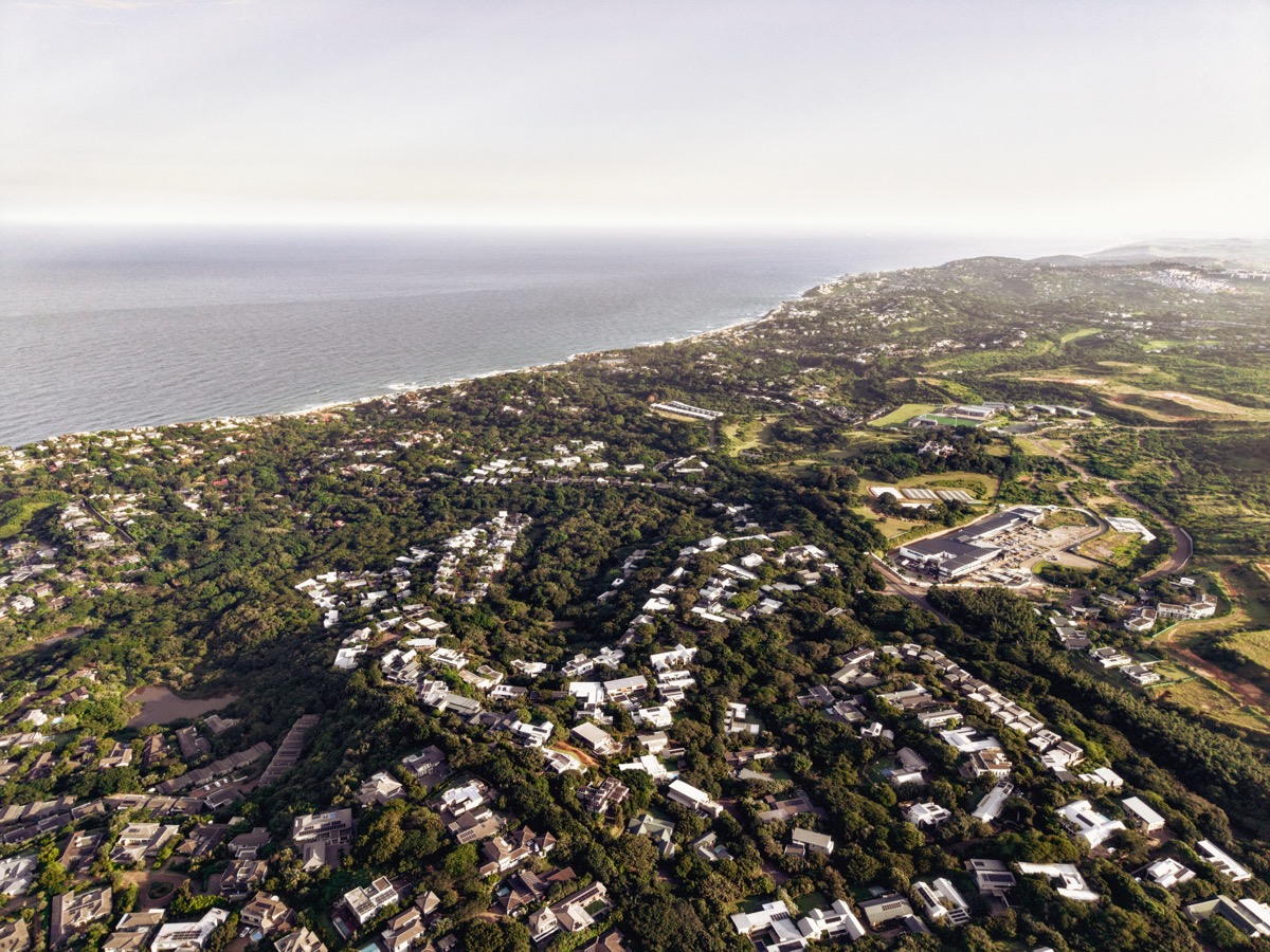 An expansive aerial view of a lush coastal town with numerous white-roofed homes nestled among dense green trees, representing platforms for coastal property management.