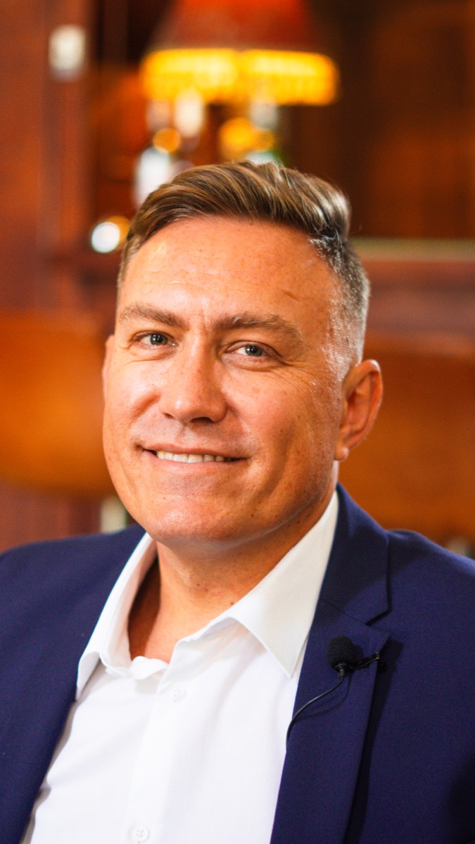 A smiling professional man in a blazer and lapel microphone, representing technical expertise and the platforms powering digital builds.