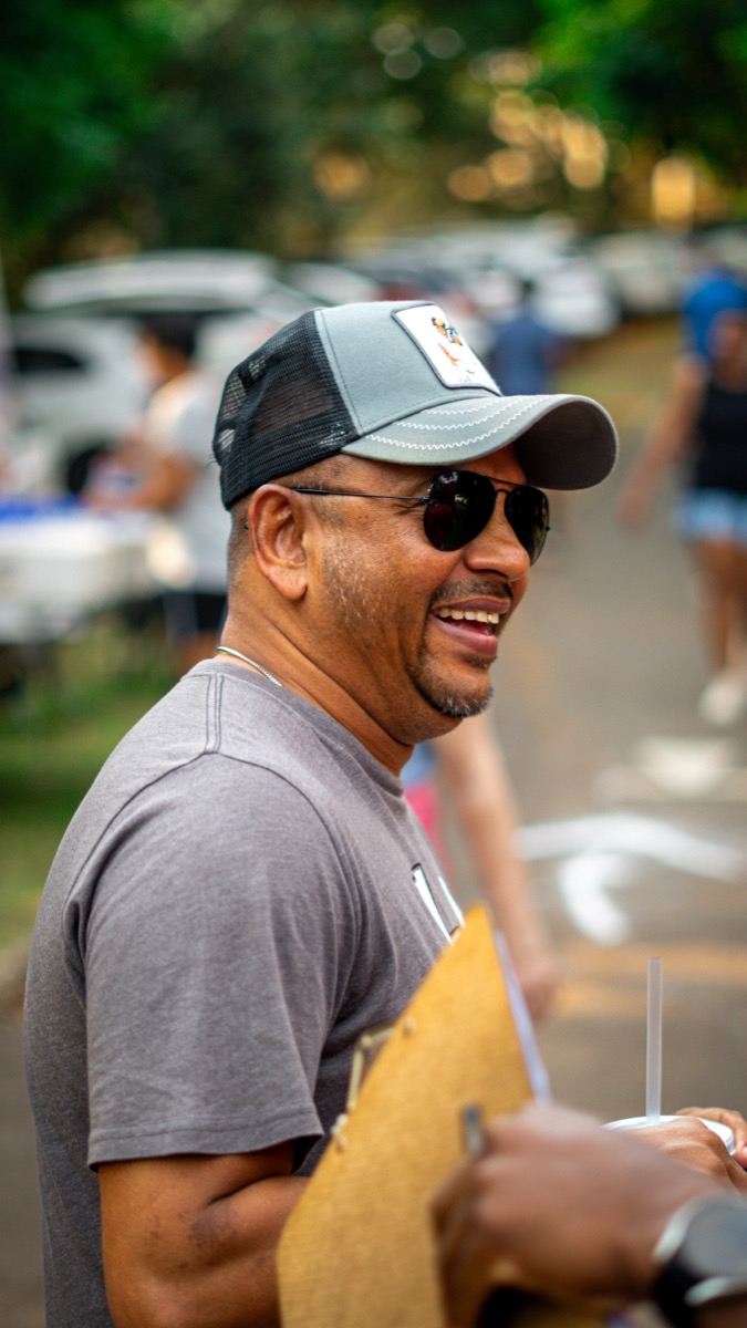 A smiling man wearing a hat and sunglasses, holding a clipboard, representing the business process and methodology from concept to delivery.