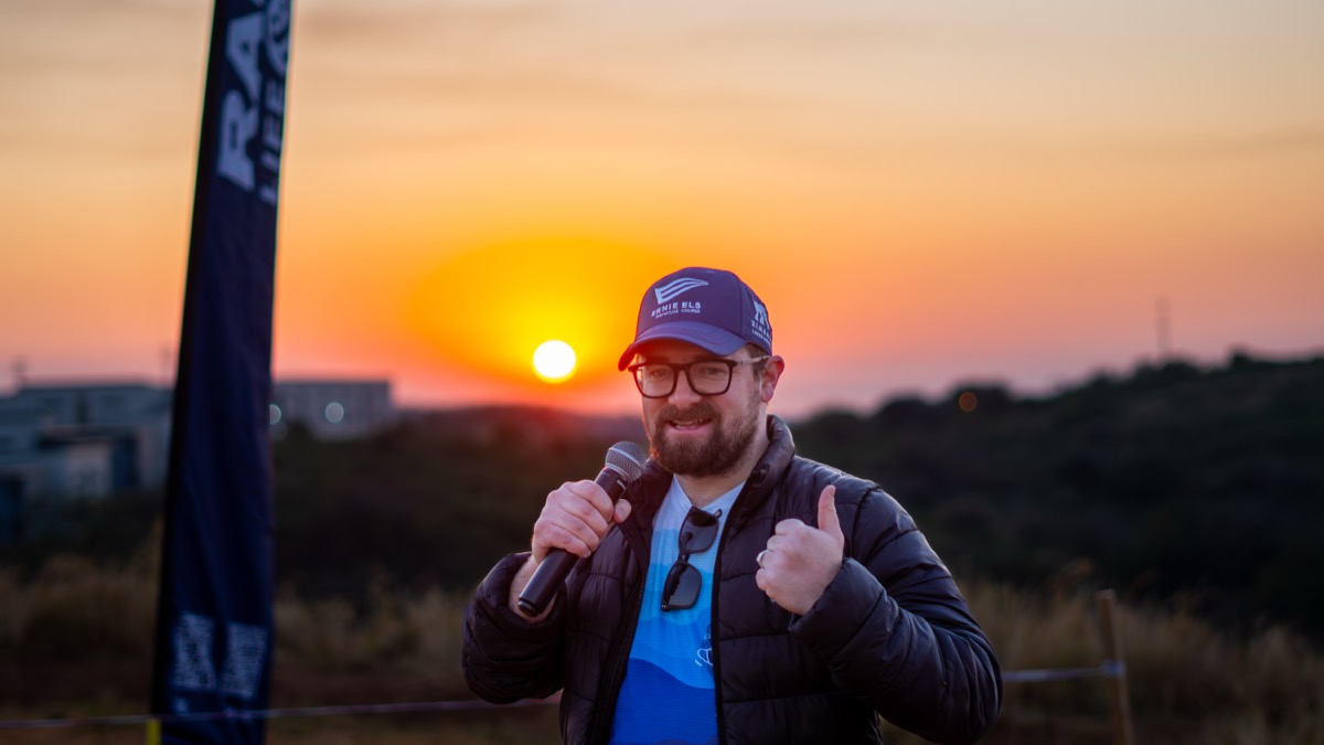 A smiling speaker giving a thumbs-up while holding a microphone against a sunset, representing performance marketing and converting attention into actionable data.