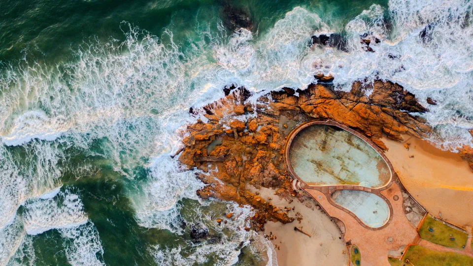 Aerial view of a tidal pool surrounded by waves and rocks.