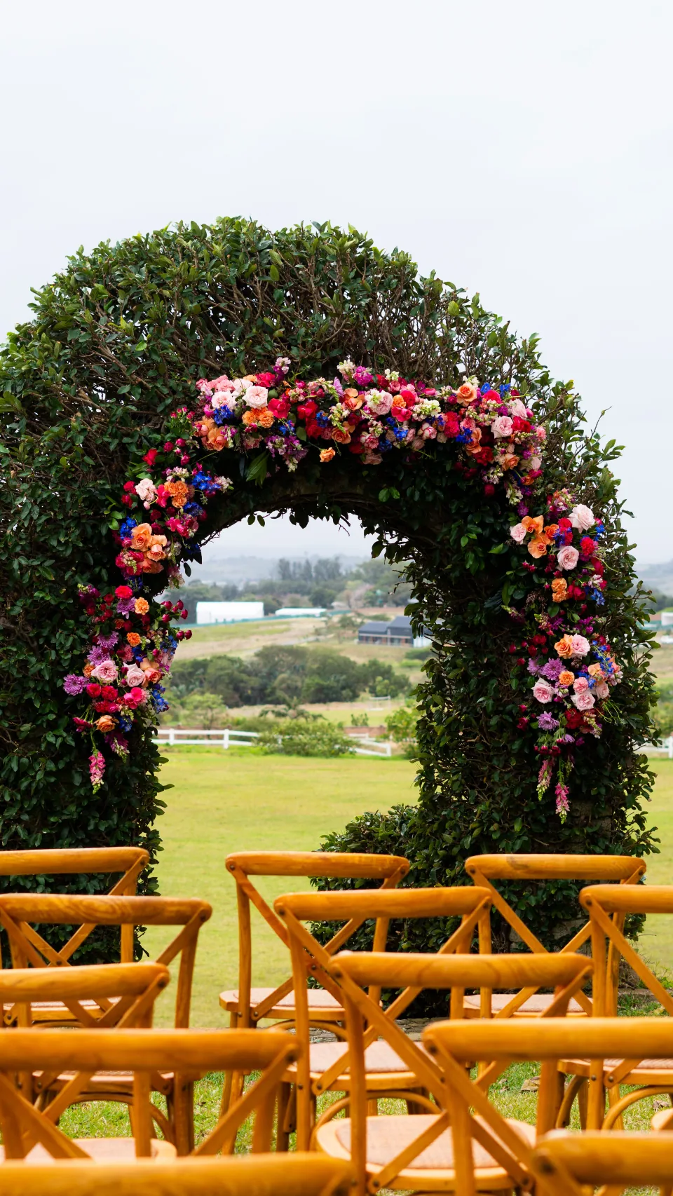 A flower-covered arch and rows of chairs at an outdoor ceremony.