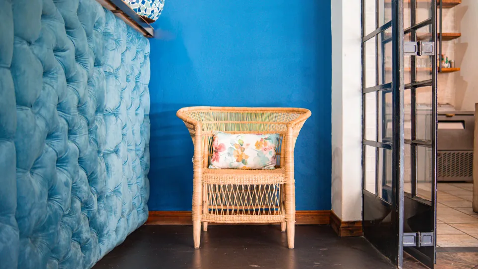 A wicker chair beside a blue upholstered wall.